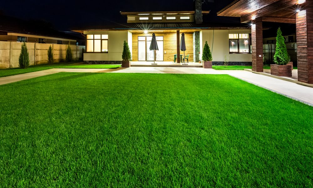 Detached luxury house at night - view from outside the rear courtyard with a green lawn.